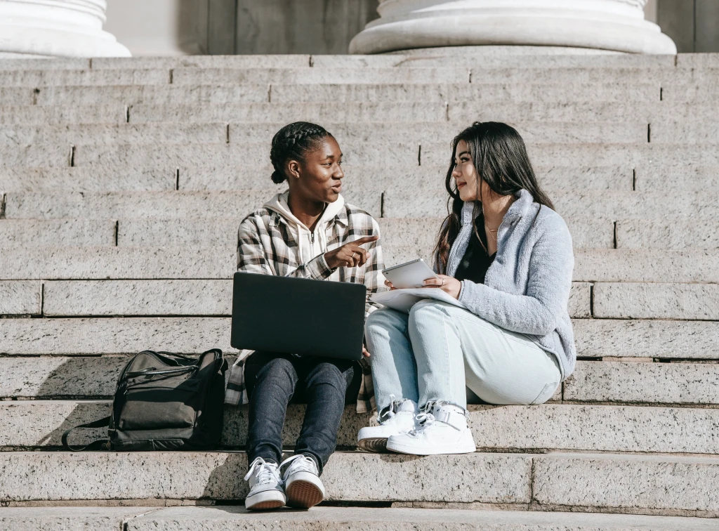 Two people sitting on stairs, with a laptop and a notepad.